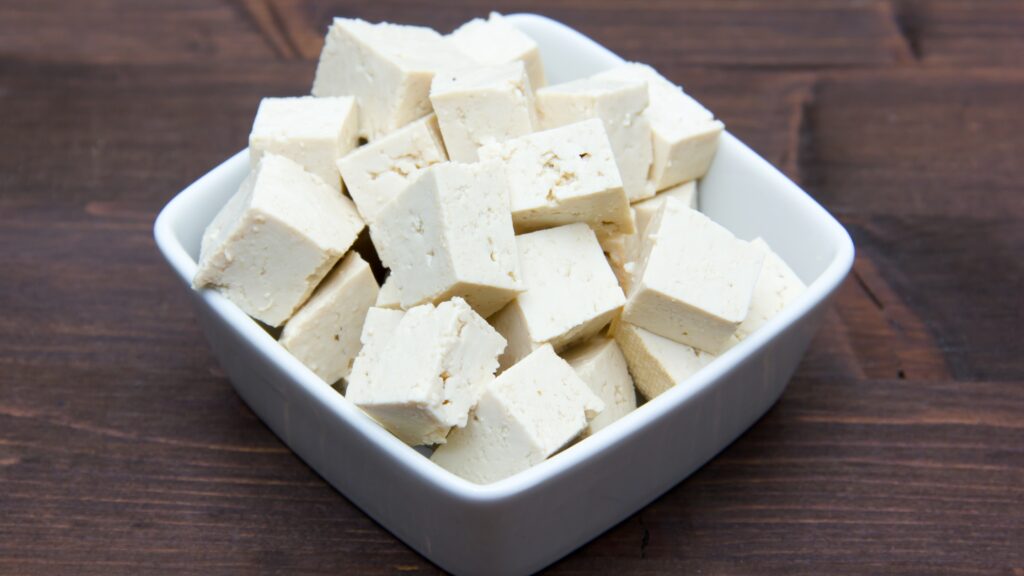 Cubes de tofu nature dans un bol blanc sur une table en bois.