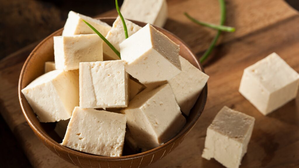 Cubes de tofu nature dans un bol en bois sur une table avec des brins de ciboulette