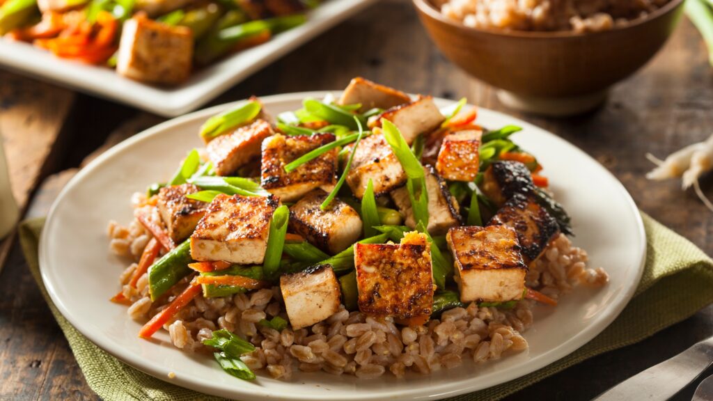 Tofu sauté avec des légumes verts sur un lit de riz dans une assiette blanche