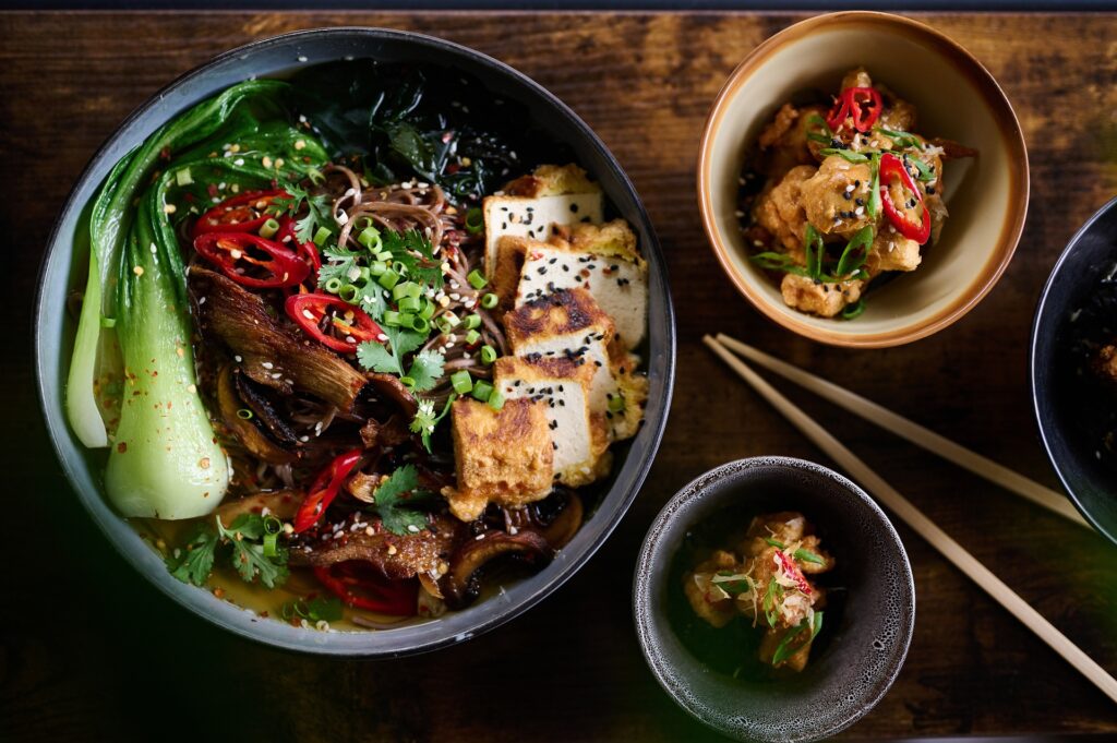 Bol de soupe asiatique avec des morceaux de tempeh grillé et légumes verts.