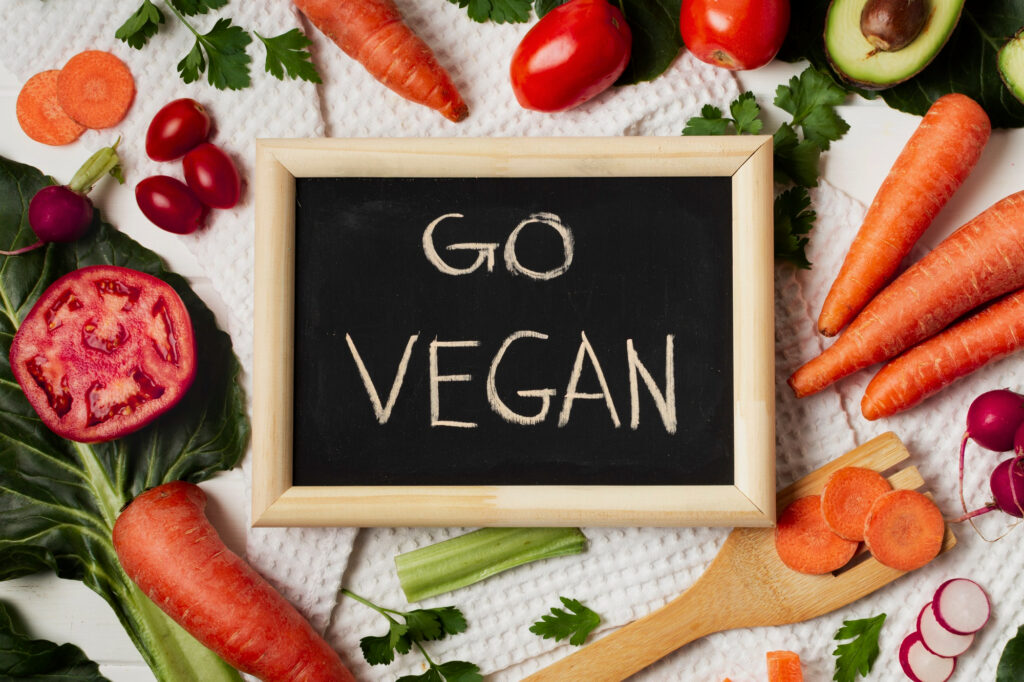 Tableau en bois avec "Go Vegan", entouré de légumes, incitant à réduire la consommation de viande.