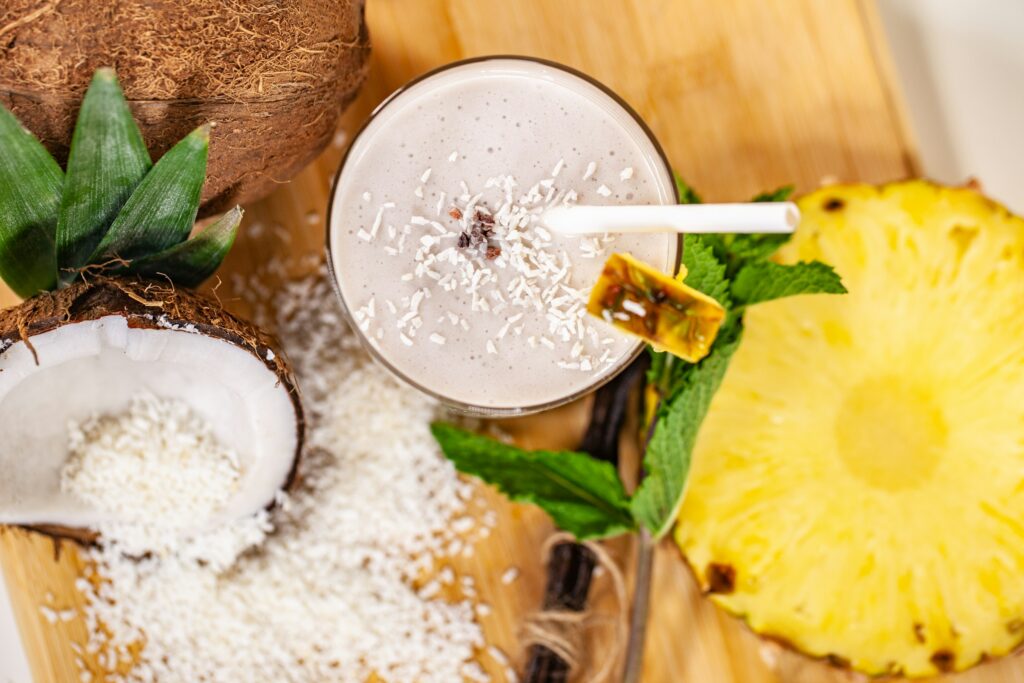 Smoothie tropical à base de protéines végétales avec coco et ananas sur une table en bois.